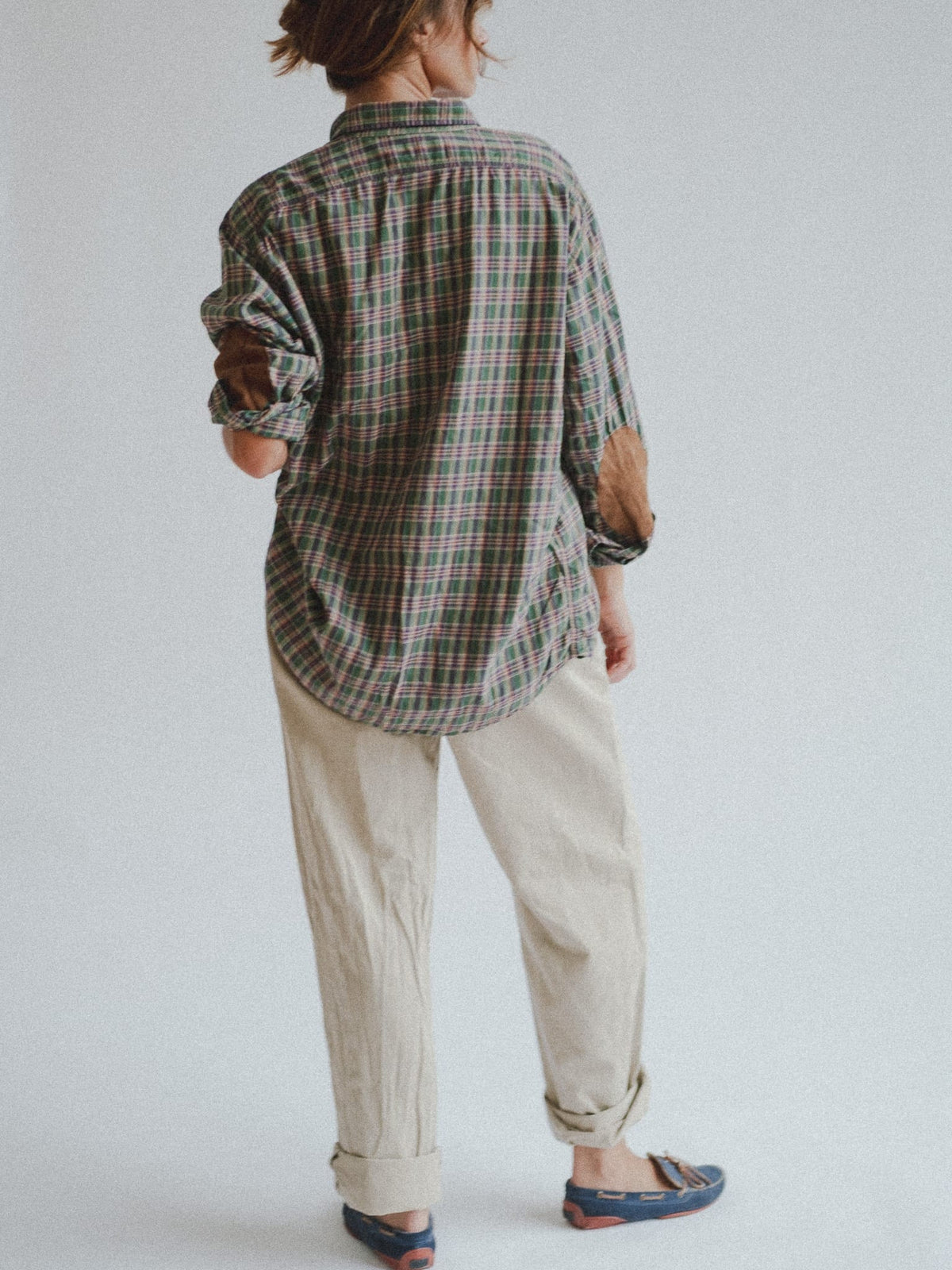 Full-cut pleated cotton chinos in pale stone, turned up at the hem, worn with a plaid shirt and driving moccasins